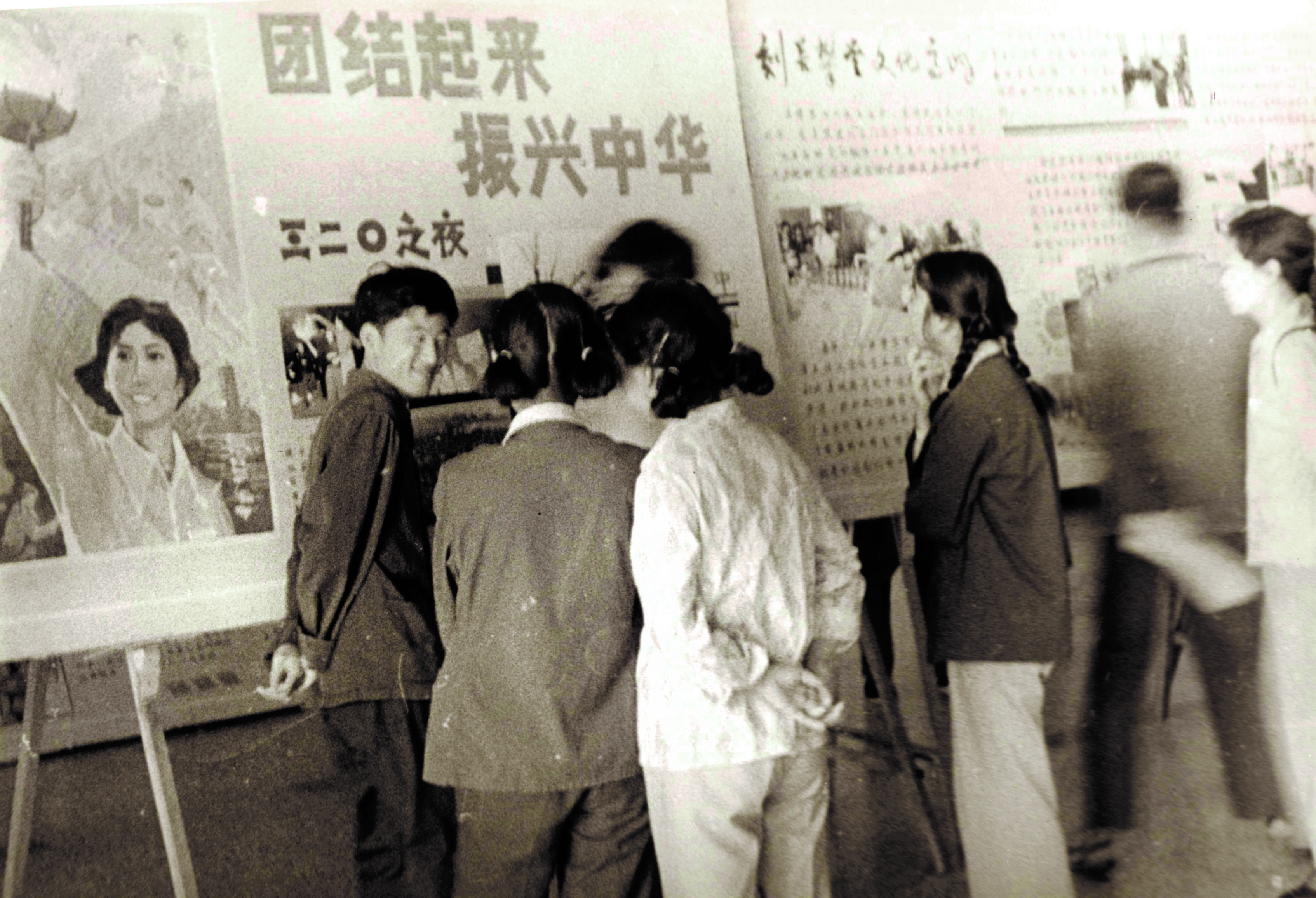 bb7d43a12e3947acac91b6e00db02137.jpg 1981年3月20日,中国男子排球队战胜南朝鲜队,取得参加世界杯排球赛的资格,北大校园沸腾了,北大学生喊出了“团结起来,振兴中华”的口号。图为北大学生在海报栏前面热烈议论.jpg